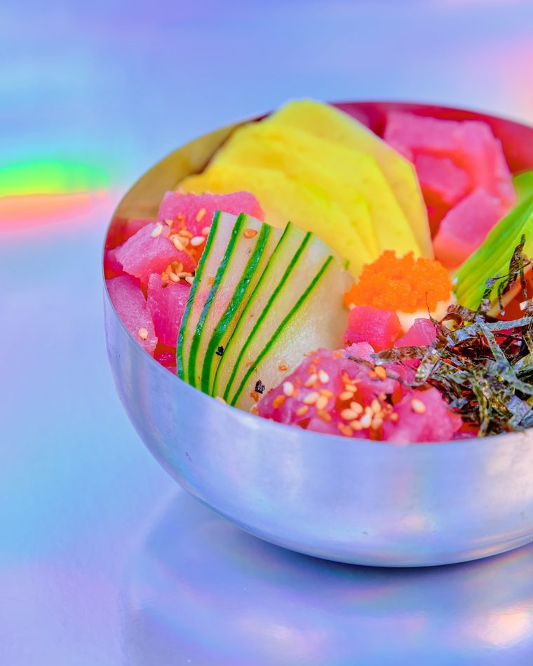 Chirashizushi numa tigela de metal, com salmão, manga, avocado, pepino e ovas, sobre fundo holográfico.