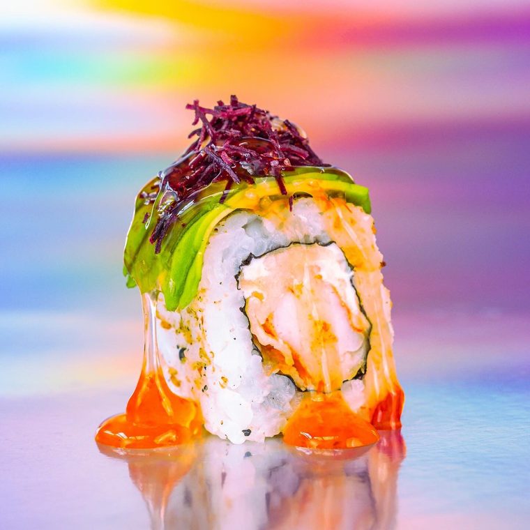 Uramaki Ebi Furai sobre fundo holográfico, coberto de avocado, beterraba crocante e um fio de molho.